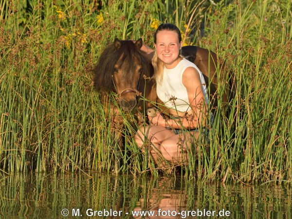 Frau mit Mini-Shetty an einem Teich im Abendlicht 