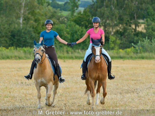 Freundinnen reiten Hand in Hand  in eine^m Stoppelfeld 