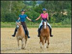 Freundinnen reiten Hand in Hand  in eine^m Stoppelfeld 