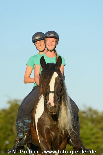 Zwei Freundinnen reiten zusammen auf einem Tinker 