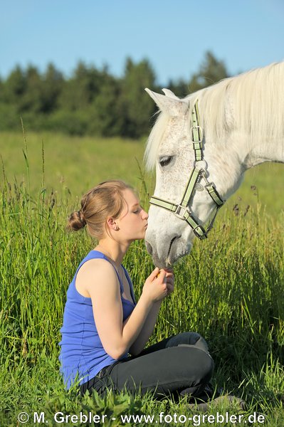 Teenager sitze in einer Wiese und küsst ihr Pony 