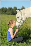 Teenager sitze in einer Wiese und küsst ihr Pony 