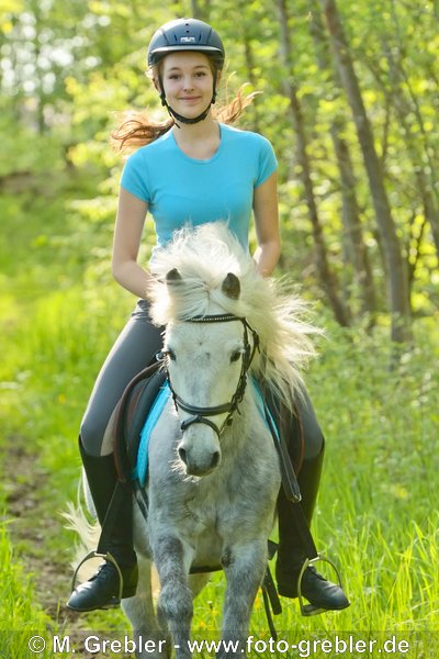 Mädchen auf Schimmel Pony reitet auf einem Waldweg 