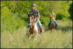 Zwei Reiterinnen galoppieren in einer Wiese, Pony und Trakehner 