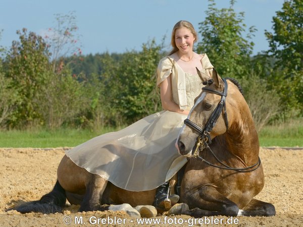 Junge Reiterin in historischem Kleid auf liegendem Lusitano-Hengst