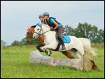 Zwei Reiterinnen auf Ponys springen gleichzeitig über einen Baumstamm 