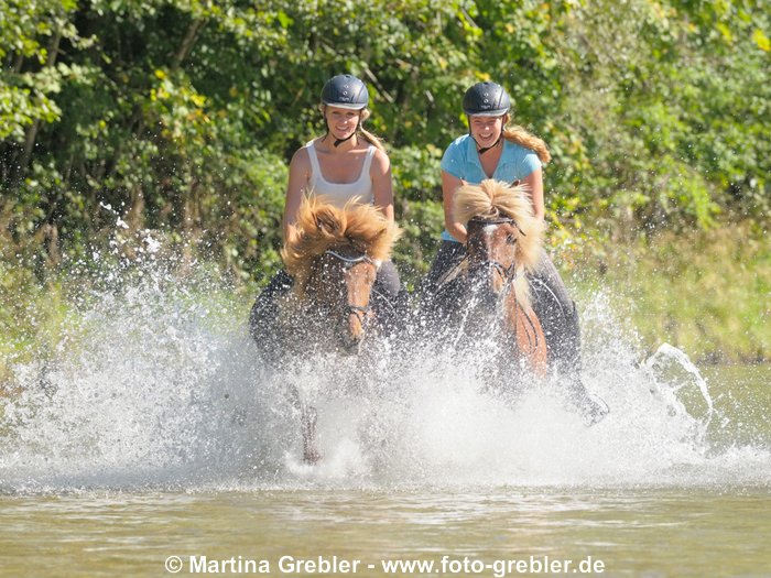 Zwei junge Reiternnen auf Isländern galoppieren in der Isar südlich von München