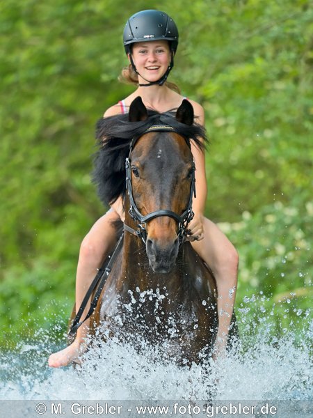 Mädchen auf Deutschem Reitpony reitet in einem Bach 