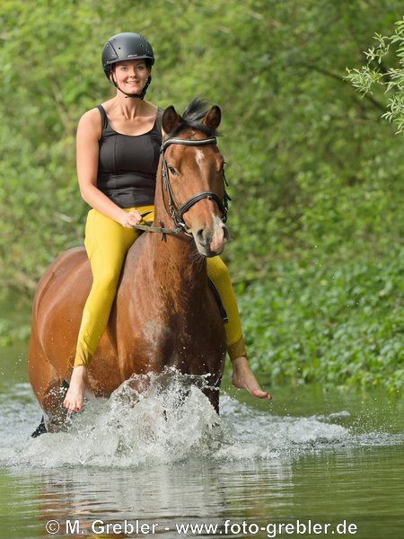 Frau reitet ohne Sattel auf Pony in einem Bach