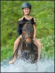 Mädchen auf Deutschem Reitpony reitet in einem Bach 