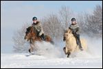 Zwei junge Reiterinnen auf Islandpferden galoppieren im Tiefschnee 