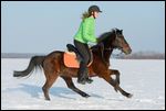 Junge Reiterin auf Reitpony galoppiert im Schnee 